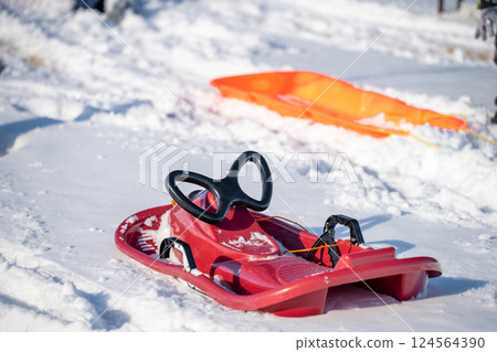 Sled resting next to a path and tracks in a snow covered hill slope. 124564390
