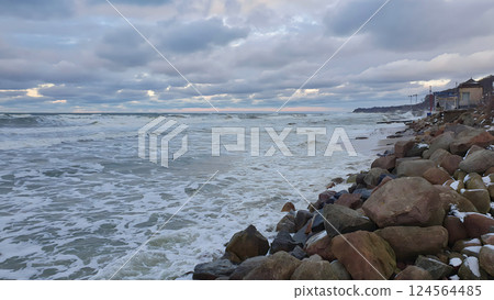 Scenic seaside landscape of severe Baltic sea coast with stormy waves rolling on boulders on empty rocky shore under dramatic sky with storm clouds at winter dusk. No people desolate seascape. 124564485