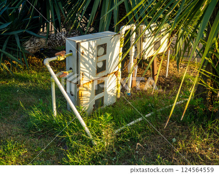 Electricity meters in the garden. Industry and nature. Iron device among palm trees 124564559