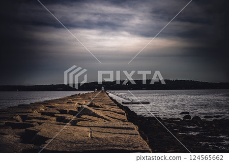 Low level view of the uneven rock path leading out to the Rockland Breakwater Lighthouse cutting through the harbor on the Gulf of Maine  124565662