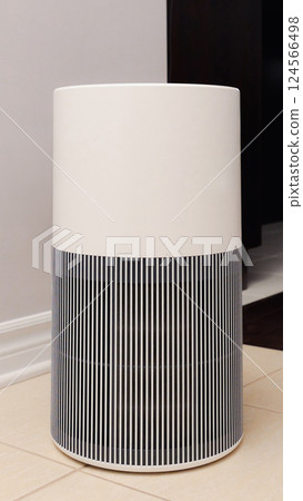 Tall round air purifier with a black top fan and a white body on a tile floor against the wall Tall round air purifier with a black top fan and a white body on a tile floor against the wall 124566498