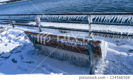 A Beautiful Wooden Bench Covered with Icicles Near the Icy Sea in a Winter Wonderland Setting A Beautiful Wooden Bench Covered with Icicles Near the Icy Sea in a Winter Wonderland Setting 124566508
