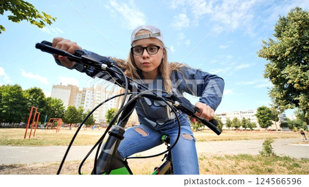 Young woman pedaling bicycle through urban green space, embodying healthy living and eco friendly urban mobility 124566596