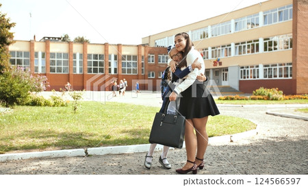 Schoolgirls embracing warmly near school entrance, displaying close bond and joyful camaraderie 124566597