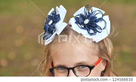 Portrait of a school girl wearing elegant white and blue bows and glasses, ready for her first day of school 124566610
