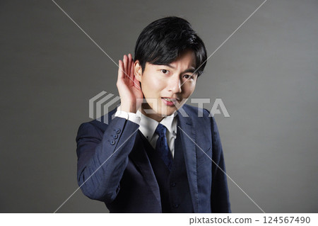 Businessman holding his hand to his ear, black background 124567490
