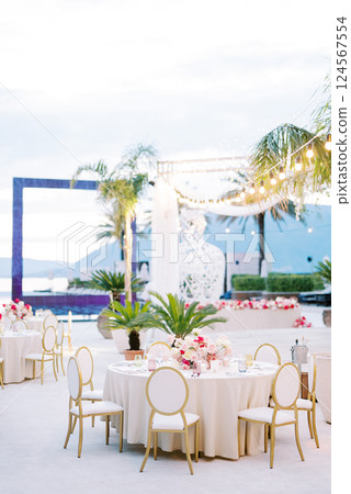 Laid festive table with a bouquet of flowers stands on a terrace with a glowing garland of light bulbs 124567554