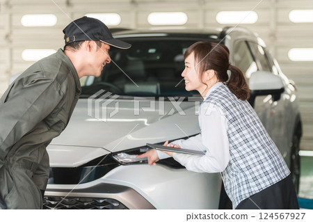 一名男汽車修理工和一名身著辦公室服裝的女前台工作人員在一輛車前交談 一名男汽車修理工和一名身著辦公室服裝的女前台工作人員在一輛車前交談 124567927