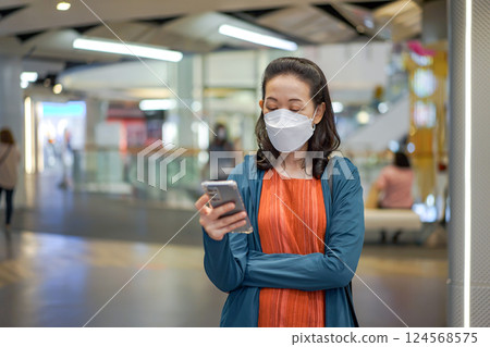 Asian Thai woman wears masks and plays mobile phone in a department or convenience store. 124568575