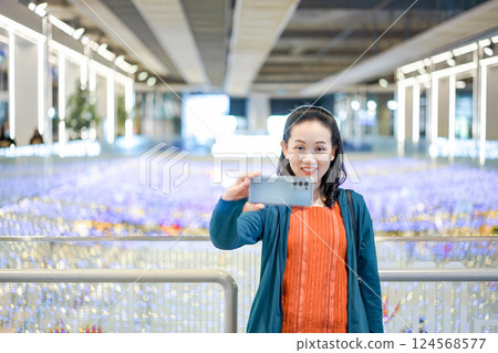 Asian Woman in green orange cloth selfies in shopping mall which is a colorful light place. Asian Woman in green orange cloth selfies in shopping mall which is a colorful light place. 124568577