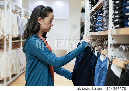Backside of a Woman wearing without face mask was selecting navy pants on a shelf in clothes shop at department stores. 124568578