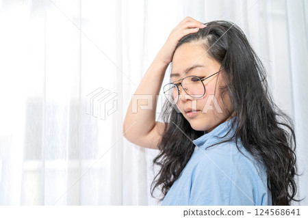 An Asian glasses woman in blue shirt poses by slicks her hair back in front of lightening curtain. An Asian glasses woman in blue shirt poses by slicks her hair back in front of lightening curtain. 124568641
