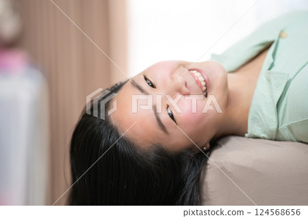 Beautiful Asian woman is lying down and playing mobile on the bed in her bedroom with a pastel green - brown color theme. 124568656