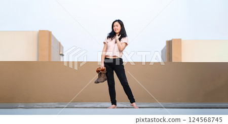 Asian woman holds brown boots in her hand and posting for photo shooting at rooftop environment at twilight time. 124568745
