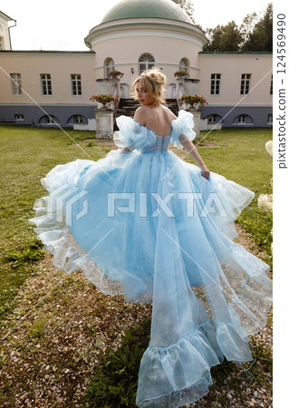 Woman in light blue ball gown runs along a path against the backdrop of a historic estate.Back view. 124569490