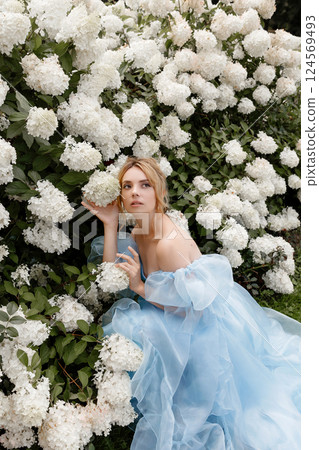 Woman in light blue ball gown poses near white lilacs 124569493