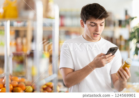 Young man customer at shop scans QR code on smoothie package using phone camera 124569901