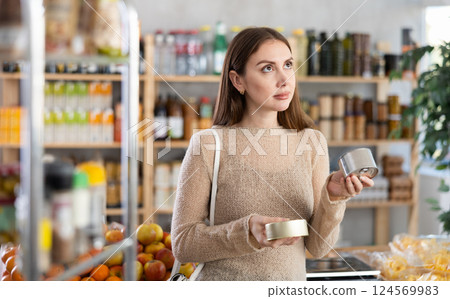 Female shopper choosing canned food in grocery store Female shopper choosing canned food in grocery store 124569983
