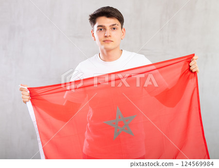 Focused young guy holding flag of Morocco Focused young guy holding flag of Morocco 124569984