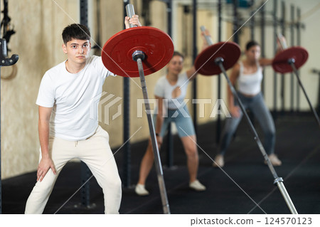 Young guy training with barbell with one arm Young guy training with barbell with one arm 124570123