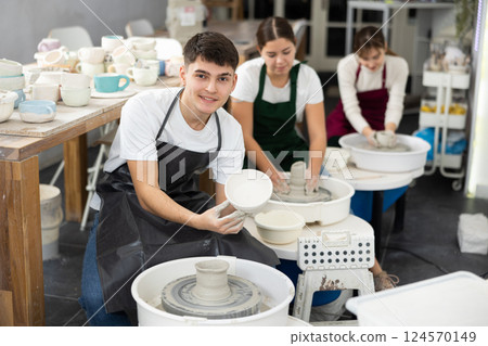 Young man holding clay bawl at pottery wheel Young man holding clay bawl at pottery wheel 124570149