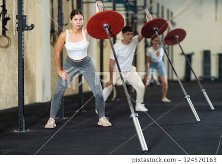Athletic young woman pumping up her arm biceps using one side of barbell 124570163