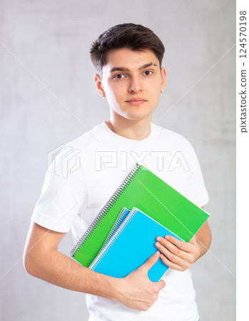 Smiling young student posing with workbooks against gray shadeless background Smiling young student posing with workbooks against gray shadeless background 124570198