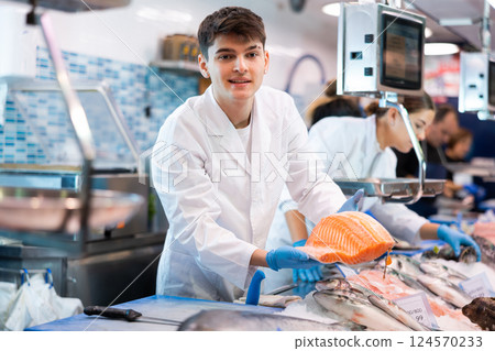 Responsive salesman demonstrating piece of salmon in fish store 124570233