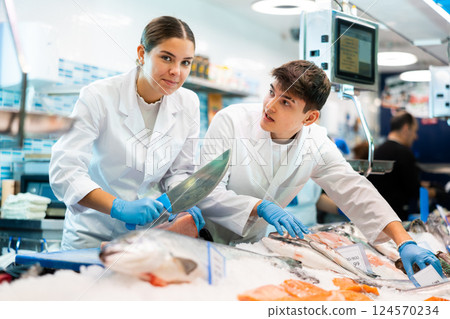 Female seller with knife cut fish in supermarket near counter Female seller with knife cut fish in supermarket near counter 124570234