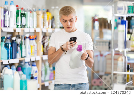 Positive young man buyer in shop holding and choosing detegrent, scan QR code Positive young man buyer in shop holding and choosing detegrent, scan QR code 124570243