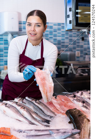 Portrait of female fishmonger showing fresh fish to woman behind counter of seafood store Portrait of female fishmonger showing fresh fish to woman behind counter of seafood store 124570244