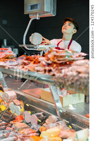 Young man butchery worker weighing sausage Young man butchery worker weighing sausage 124570245