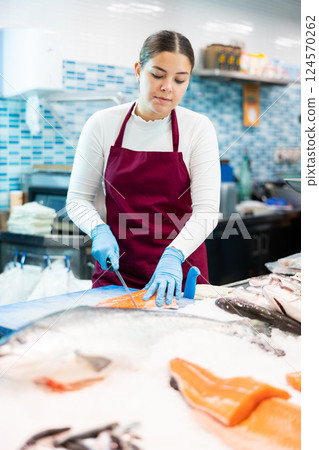 Female seller with knife cut fish in supermarket near counter 124570262