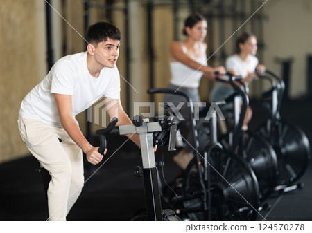 Young guy doing sports on a stationary bike in gym Young guy doing sports on a stationary bike in gym 124570278