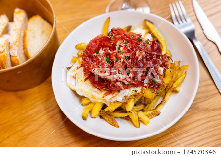 Fried eggs cooked spanish style with potatoes and slices of hamon with sliced bread glass of wine and cutlery Fried eggs cooked spanish style with potatoes and slices of hamon with sliced bread glass of wine and cutlery 124570346