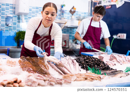 Female seller standing near counter offering fresh fish striped red mullet Female seller standing near counter offering fresh fish striped red mullet 124570351