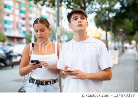 Modern man and woman strolling together and phubbing 124570357