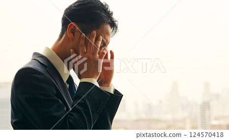 A male business person worries while looking at the city from the office window A male business person worries while looking at the city from the office window 124570418