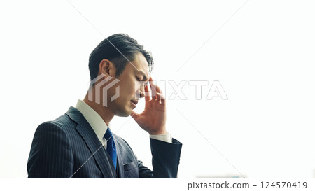 A male business person worries while looking at the city from the office window 124570419