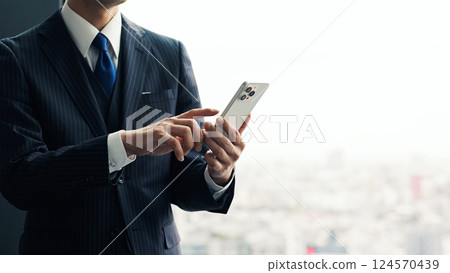 Male business person using a smartphone in an office with a city in the background Male business person using a smartphone in an office with a city in the background 124570439
