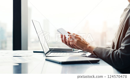 A female business person working with a laptop and smartphone in an urban office building 124570478