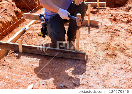 Construction worker is driving stakes into ground to establish foundation layout 124570846