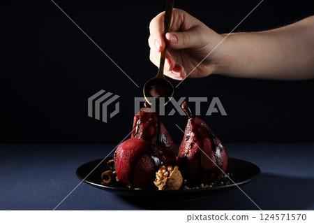Pears in wine on plate and spoon in hand on dark blue background 124571570