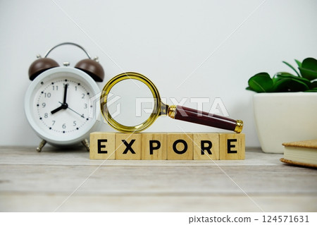 Magnifying glass and alarm clock with wooden blocks alphabet letters EXPORE text message on wooden background 124571631