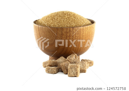 A rustic wooden bowl overflows with raw brown sugar accompanied by neatly arranged sugar cubes. A rustic wooden bowl overflows with raw brown sugar accompanied by neatly arranged sugar cubes. 124572758