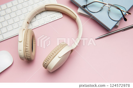 Wireless headphones, keyboard, computer mouse, eyeglasses, pen and notebooks on pink background 124572978