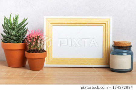 Empty frame mockup with cacti and blue jar on wooden table 124572984