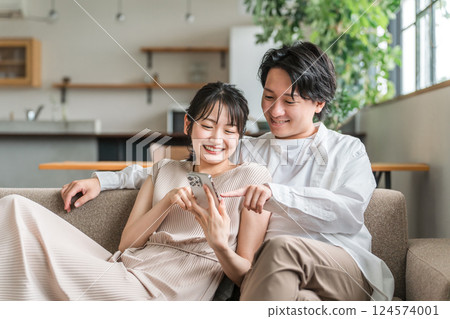 一對年輕的日本夫婦在客廳看著他們的智慧型手機（皮膚） 124574001