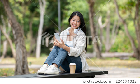 A woman looking happily at her notebook as she figure something out while sitting on park sidewalk A woman looking happily at her notebook as she figure something out while sitting on park sidewalk 124574022