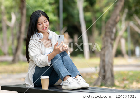 A woman looking happily at her notebook as she figure something out while sitting on park sidewalk 124574023